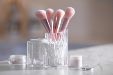 Photo of Cotton buds, pads and makeup brushes in transparent holders on light table