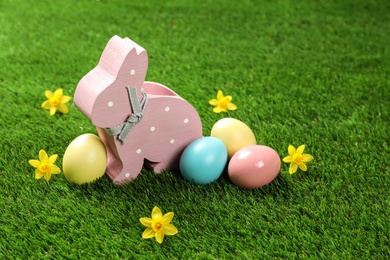 Cute wooden Easter bunny and dyed eggs on green grass