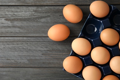 Photo of Raw chicken eggs in ceramic holder on wooden background, top view. Space for text