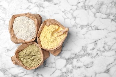 Photo of Paper bags with different types of flour on marble background