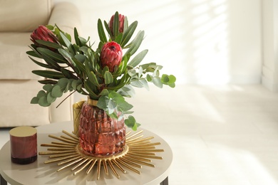 Vase with bouquet of beautiful Protea flowers on table in room