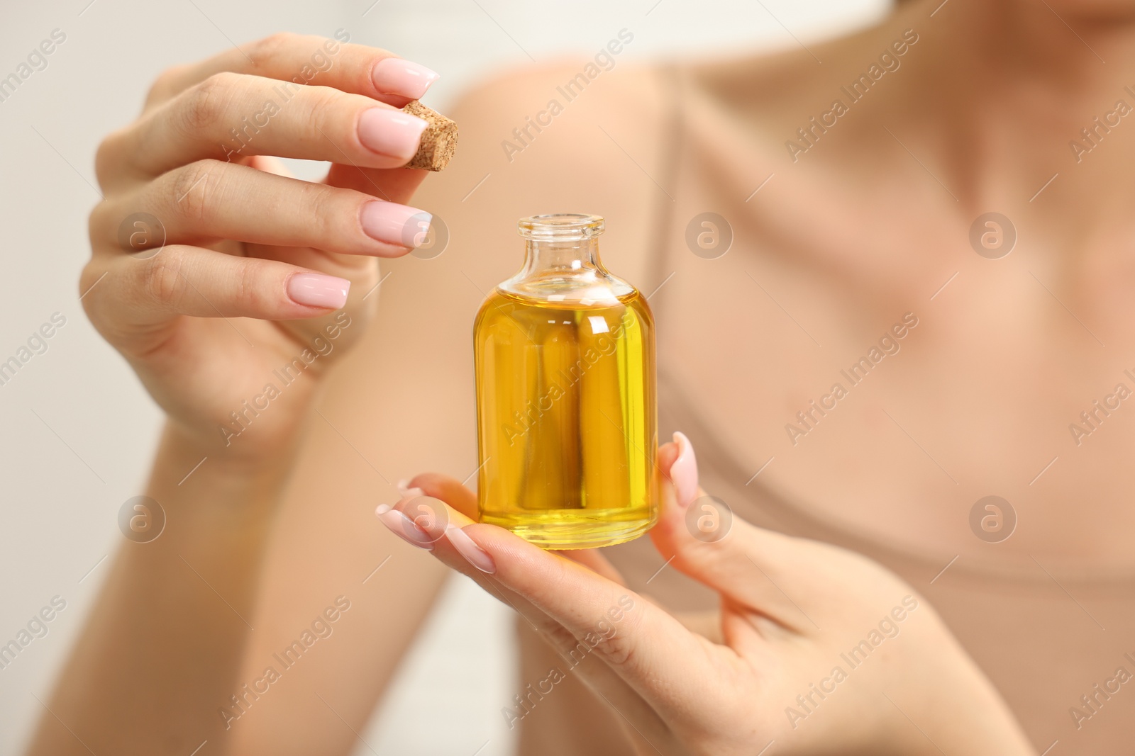 Photo of Aromatherapy. Woman with bottle of essential oil on light background, closeup