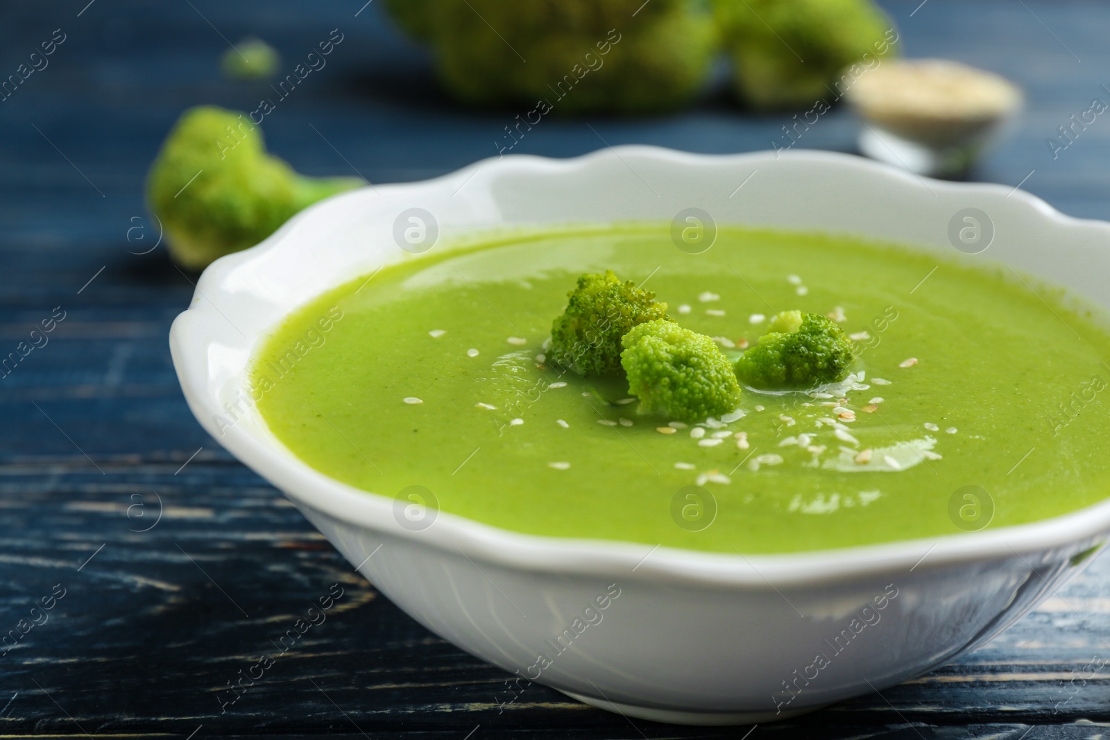 Photo of Bowl of broccoli cream soup with sesame seeds served on blue wooden table, closeup