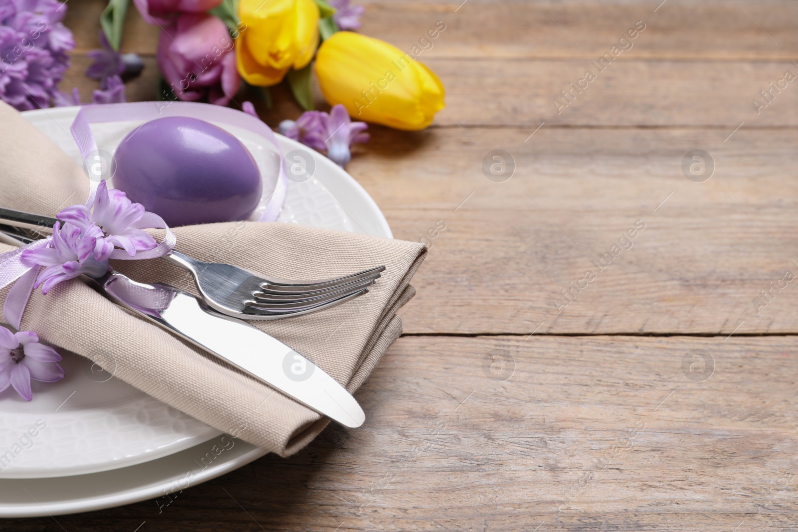 Photo of Festive Easter table setting with painted egg and flowers on wooden background, closeup. Space for text