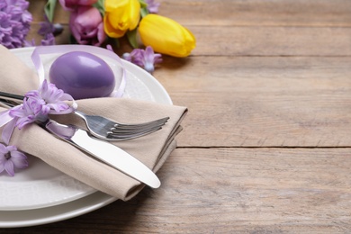 Festive Easter table setting with painted egg and flowers on wooden background, closeup. Space for text