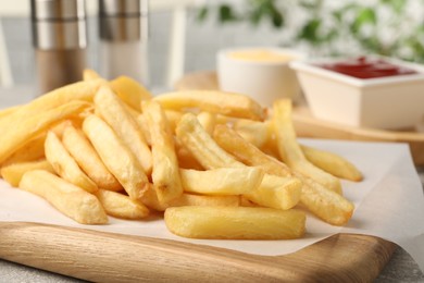 Photo of Wooden board with delicious french fries on table, closeup