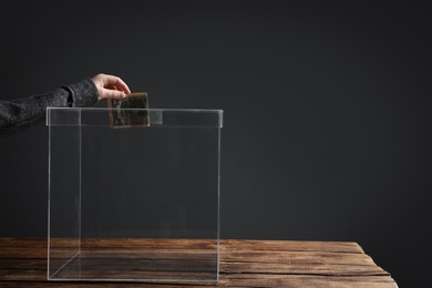 Woman putting money into donation box on table against grey background, closeup. Space for text