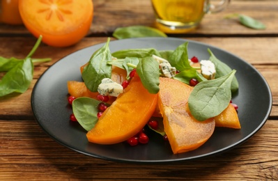Photo of Delicious persimmon salad served on wooden table, closeup