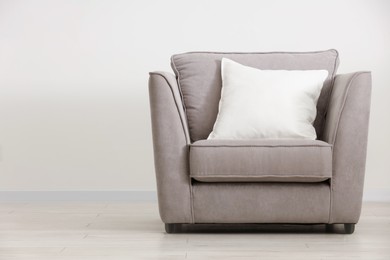 Photo of Soft white pillow on armchair near light wall indoors, space for text