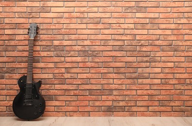Photo of Modern electric guitar near red brick wall indoors. Space for text