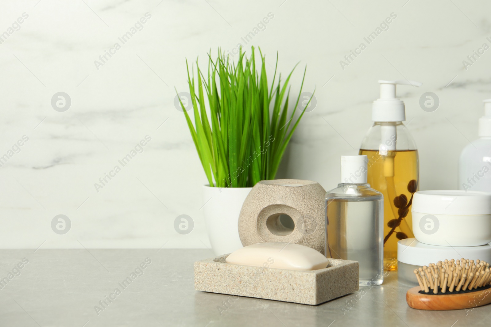 Photo of Brush and personal care products on gray table near white marble wall, space for text