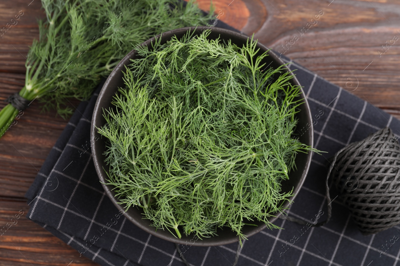 Photo of Bowl of fresh dill and spool of thread on wooden table, flat lay