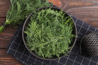 Photo of Bowl of fresh dill and spool of thread on wooden table, flat lay