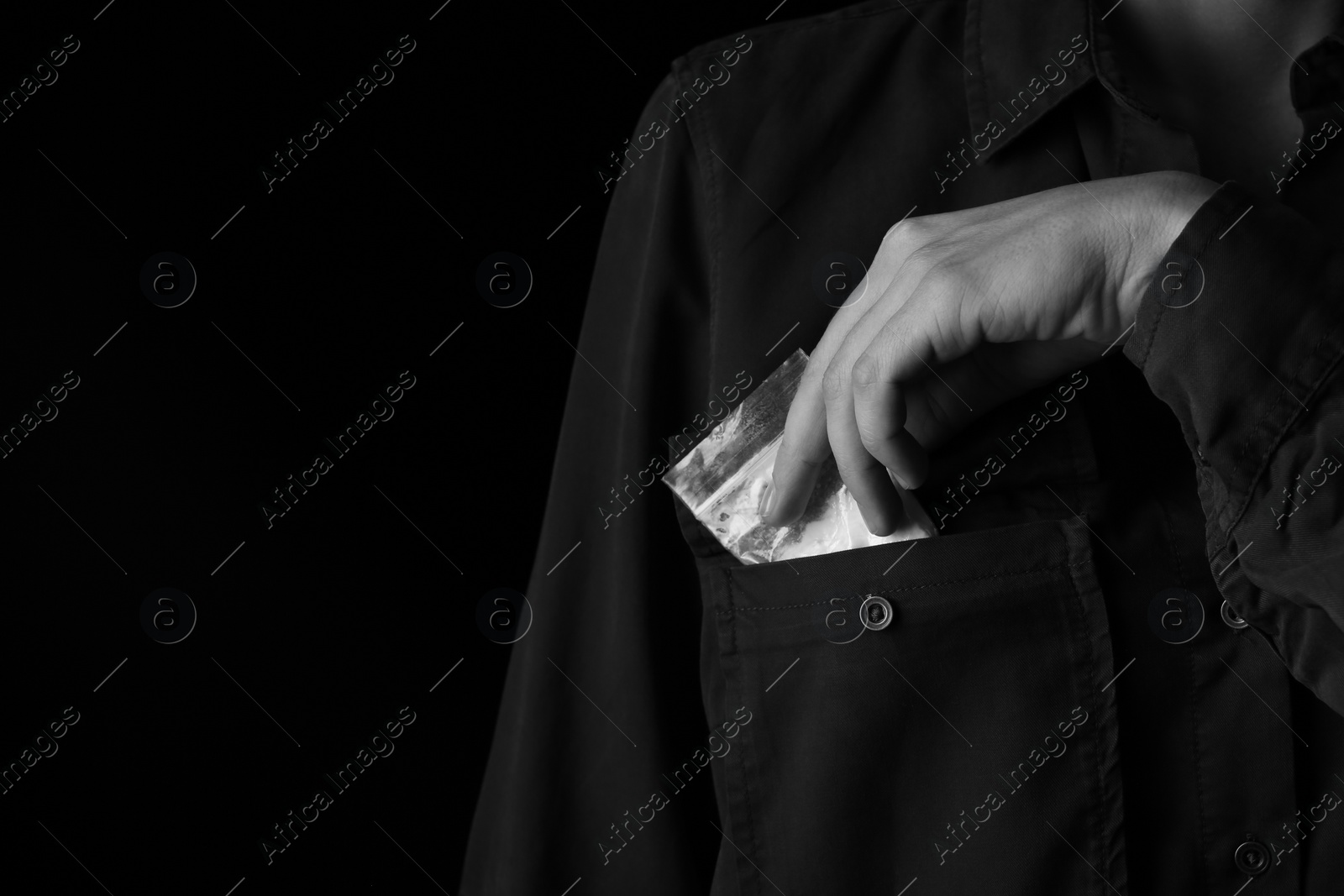 Photo of Drug dealer taking bag with cocaine out of pocket on black background, closeup. Space for text