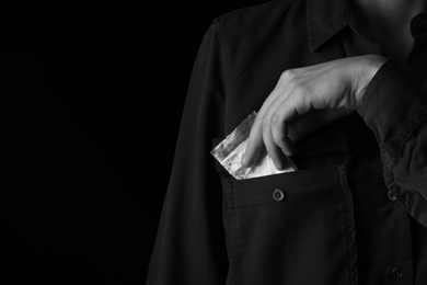 Photo of Drug dealer taking bag with cocaine out of pocket on black background, closeup. Space for text
