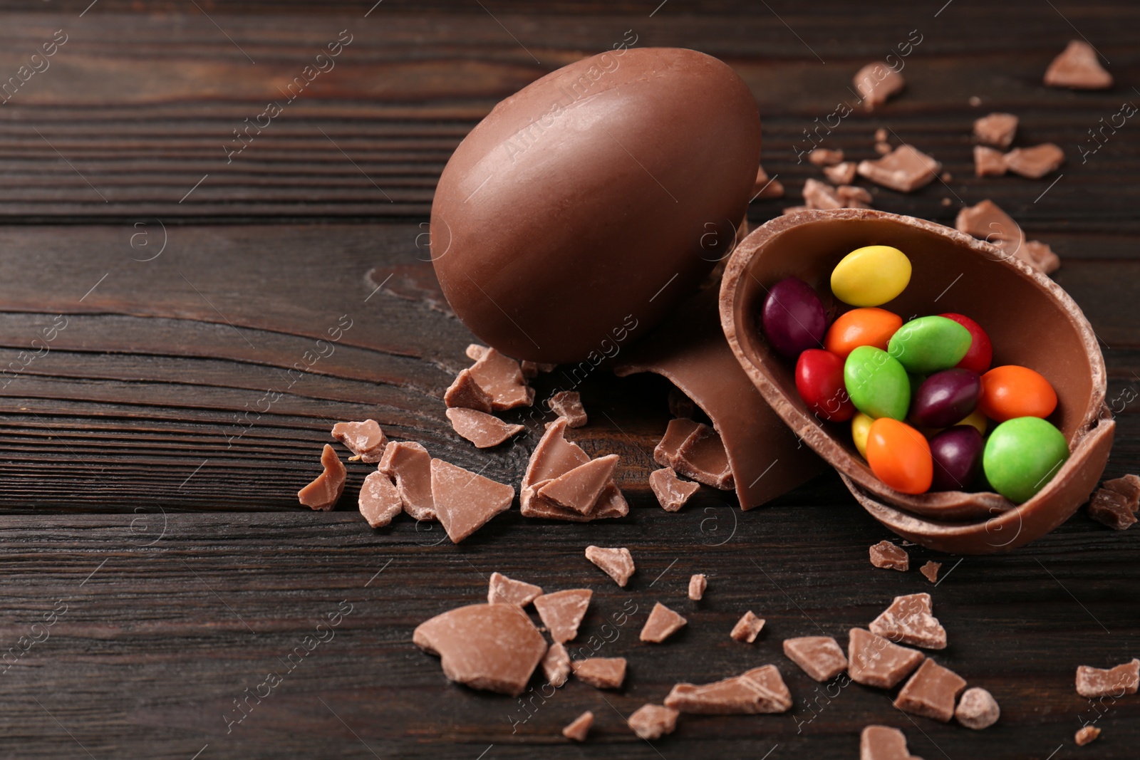 Photo of Broken and whole chocolate eggs with sweets on wooden table