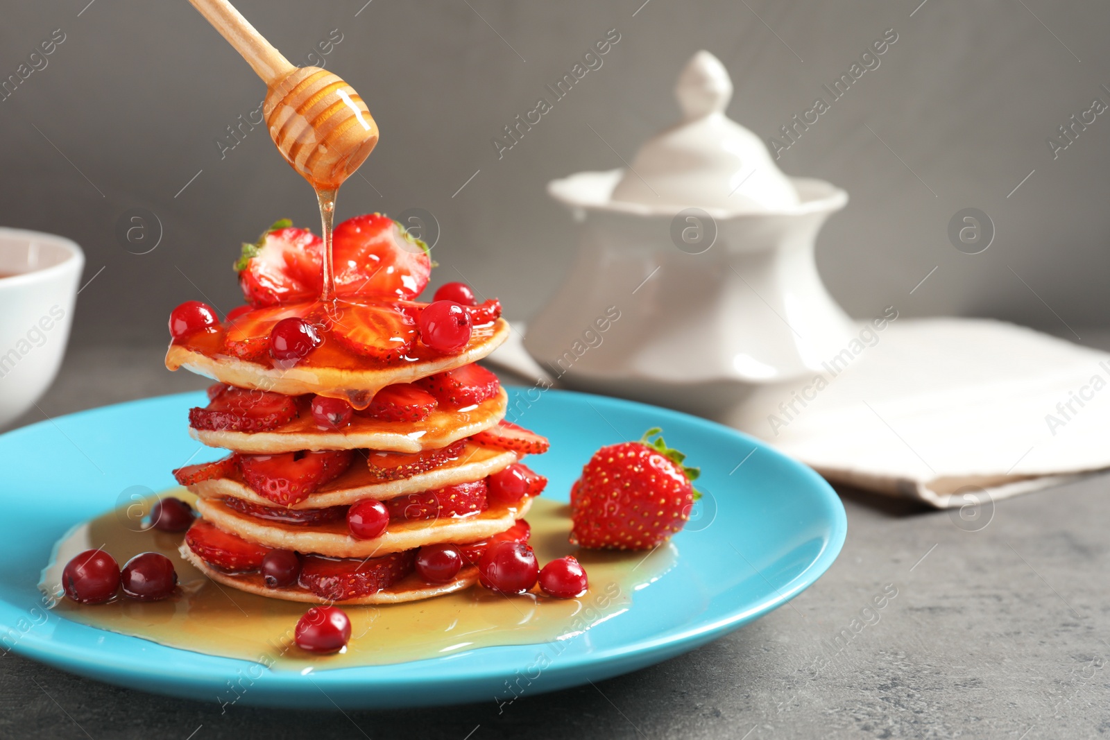 Photo of Pouring honey onto tasty pancakes with berries on plate