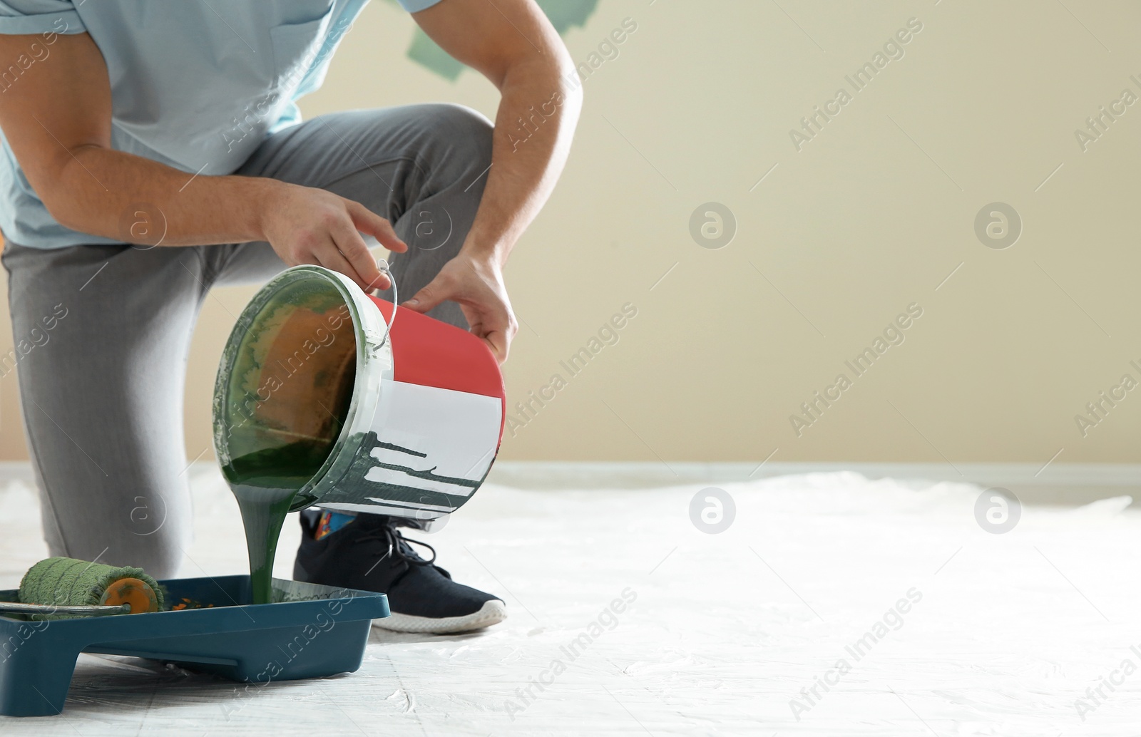 Photo of Young man pouring paint from bucket into tray indoors, closeup with space for text. Home repair