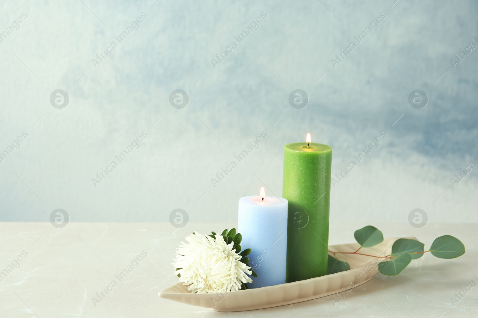 Photo of Candles with floral decor on table against color background