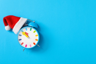 Photo of Alarm clock in Santa hat on light blue background, top view with space for text. New Year countdown