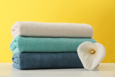Photo of Stack of soft clean towels with beautiful flower on table against color background