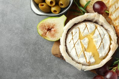 Photo of Tasty baked brie cheese and products on grey table, flat lay. Space for text