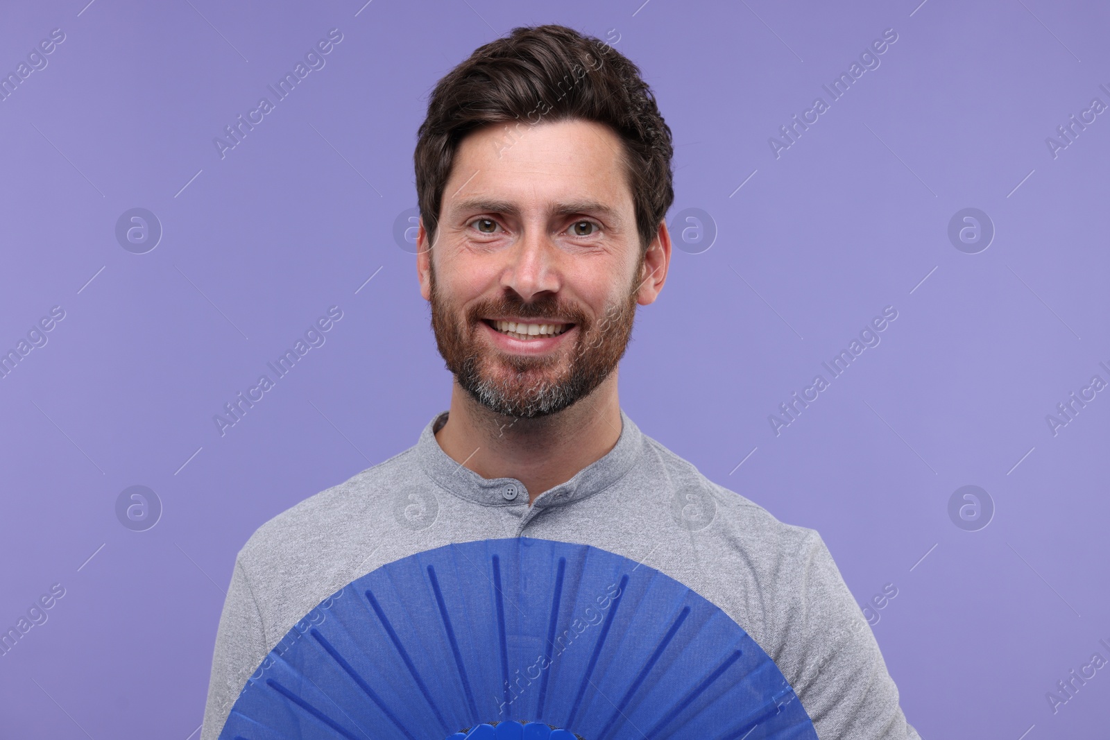 Photo of Happy man holding hand fan on purple background