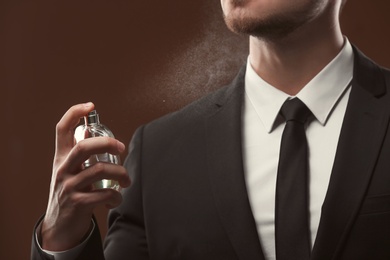 Photo of Handsome man in suit using perfume on dark background, closeup