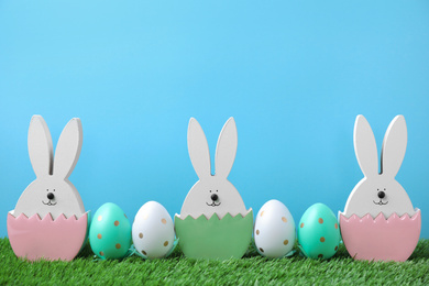 Photo of Easter bunny figures and dyed eggs on green grass against light blue background