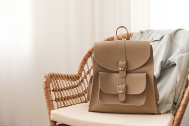 Photo of Stylish beige backpack and jacket on wicker chair indoors, space for text