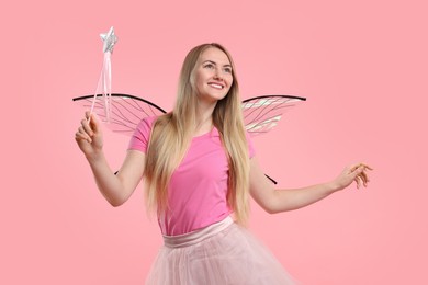 Photo of Beautiful girl in fairy costume with wings and magic wand on pink background