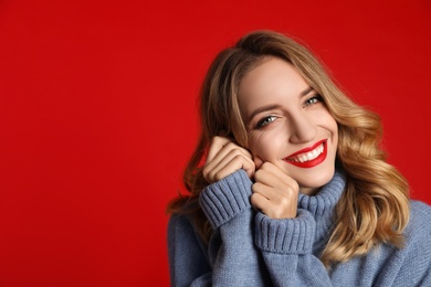 Photo of Happy young woman wearing warm sweater on red background, space for text. Christmas celebration