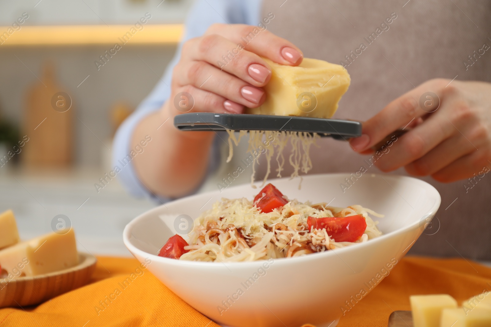 Photo of Woman grating cheese onto delicious pasta at table in kitchen, closeup