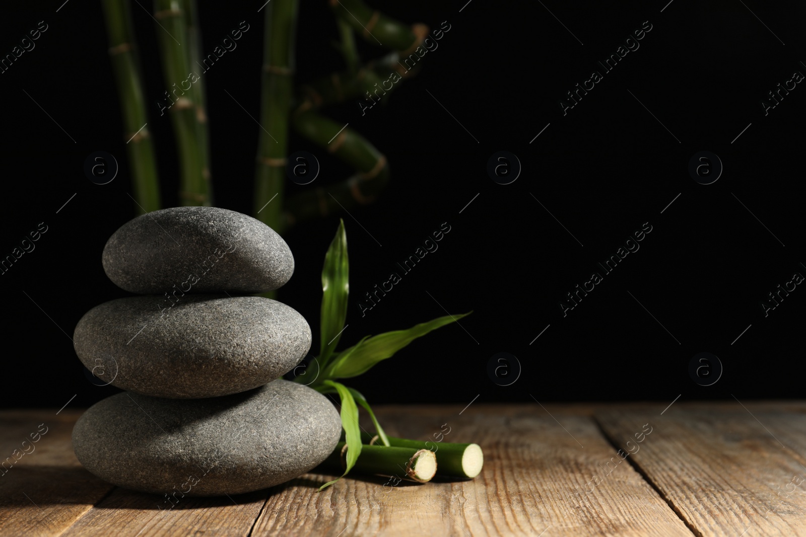 Photo of Spa stones and bamboo stems on wooden table against dark background, space for text
