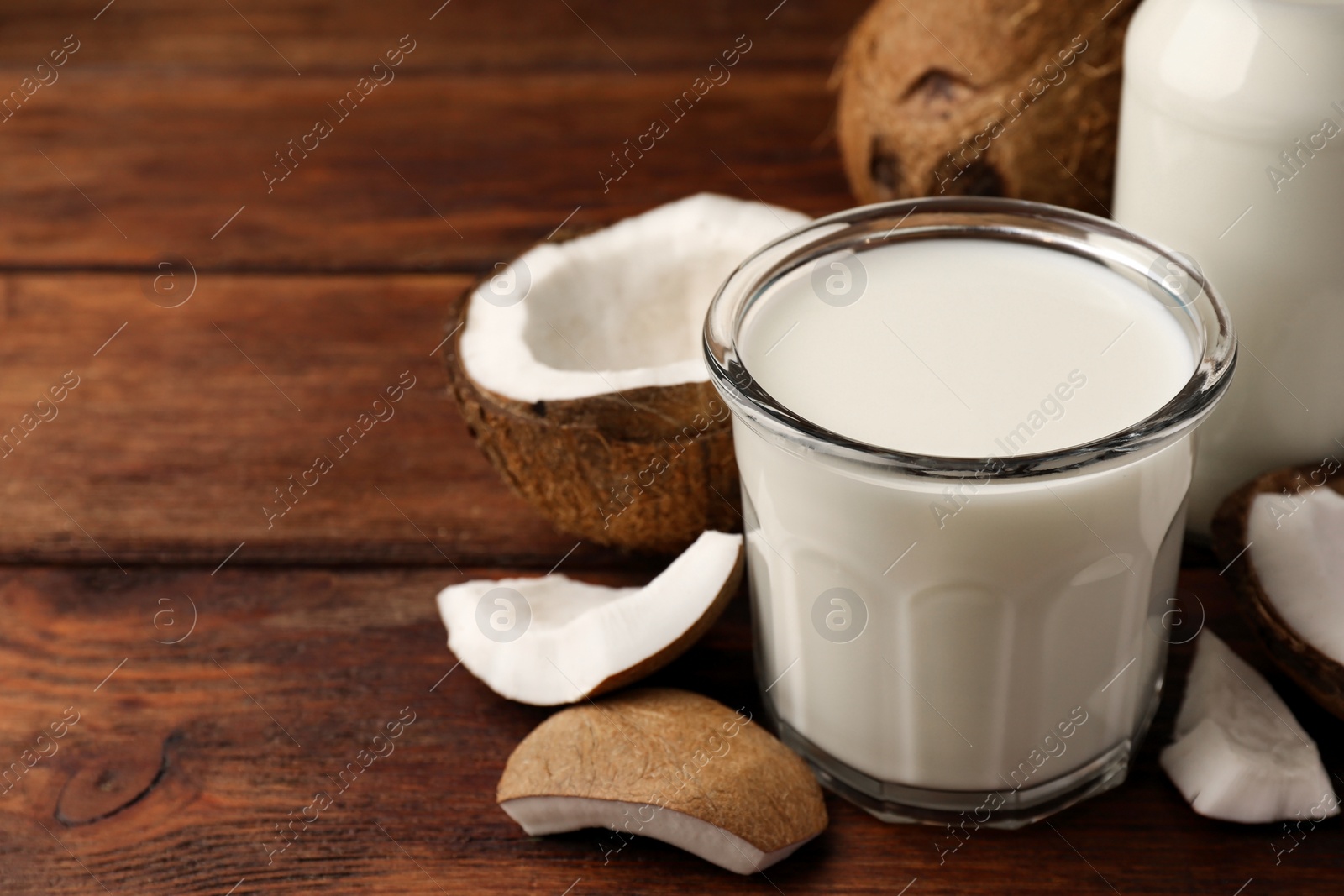 Photo of Glass of delicious vegan milk and coconut pieces on wooden table, space for text