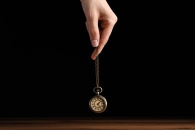 Photo of Psychotherapist with pendulum on black background, closeup. Hypnotherapy session