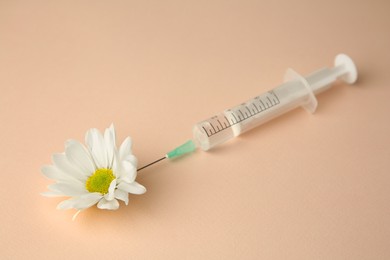 Photo of Medical syringe and beautiful chrysanthemum flower on beige background, closeup