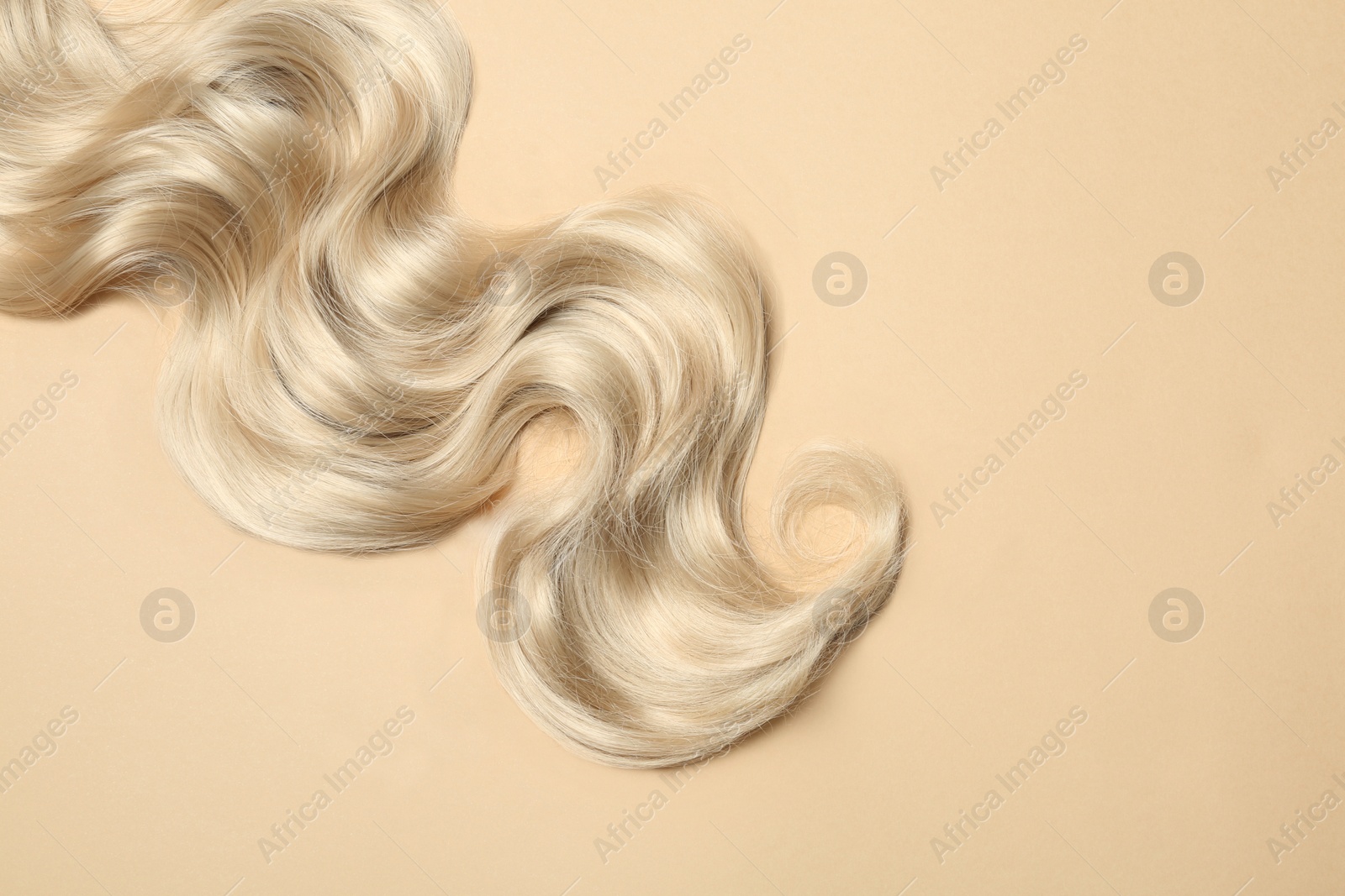 Photo of Lock of blonde wavy hair on color background, top view. Space for text