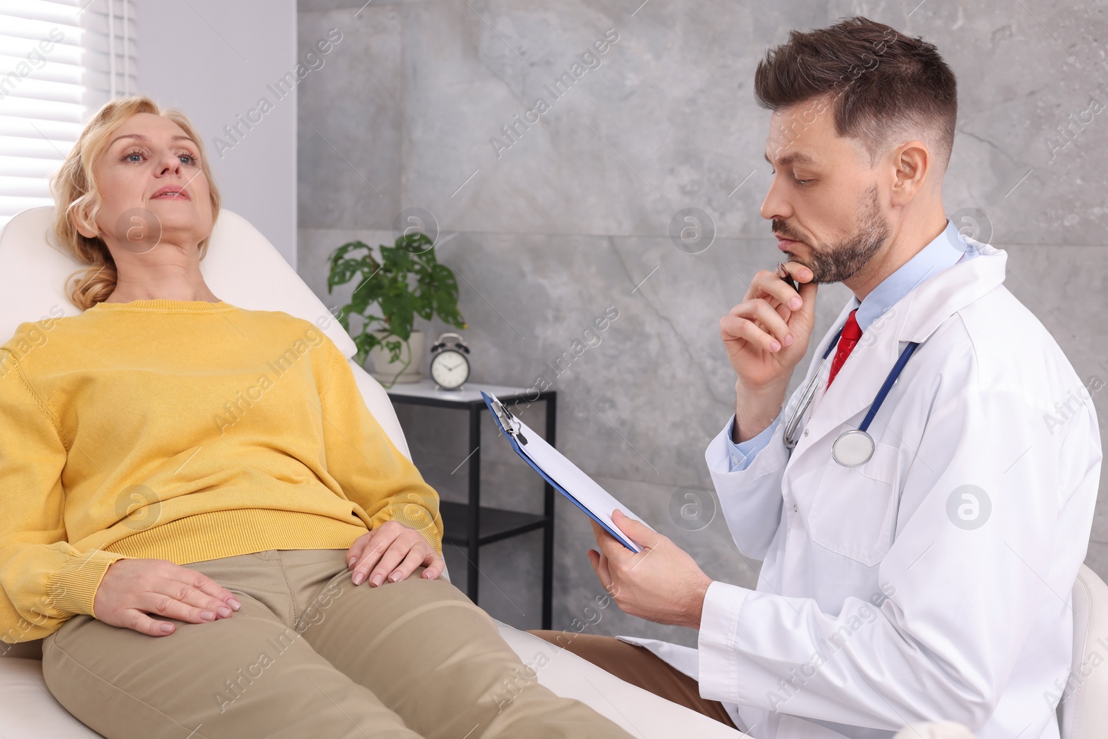 Photo of Doctor with clipboard consulting patient in clinic