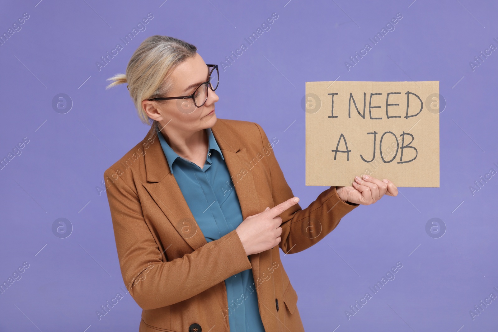 Photo of Unemployed senior woman pointing at cardboard sign with phrase I Need A Job on purple background