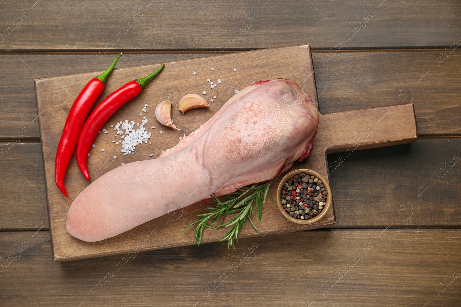 Photo of Raw beef tongue, peppercorns, garlic, salt, rosemary and chili peppers on wooden table, top view