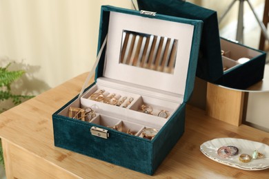 Photo of Elegant jewelry box with beautiful bijouterie and wristwatch near mirror on wooden table in room