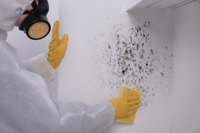 Woman in protective suit and rubber gloves removing mold from wall with rag, closeup