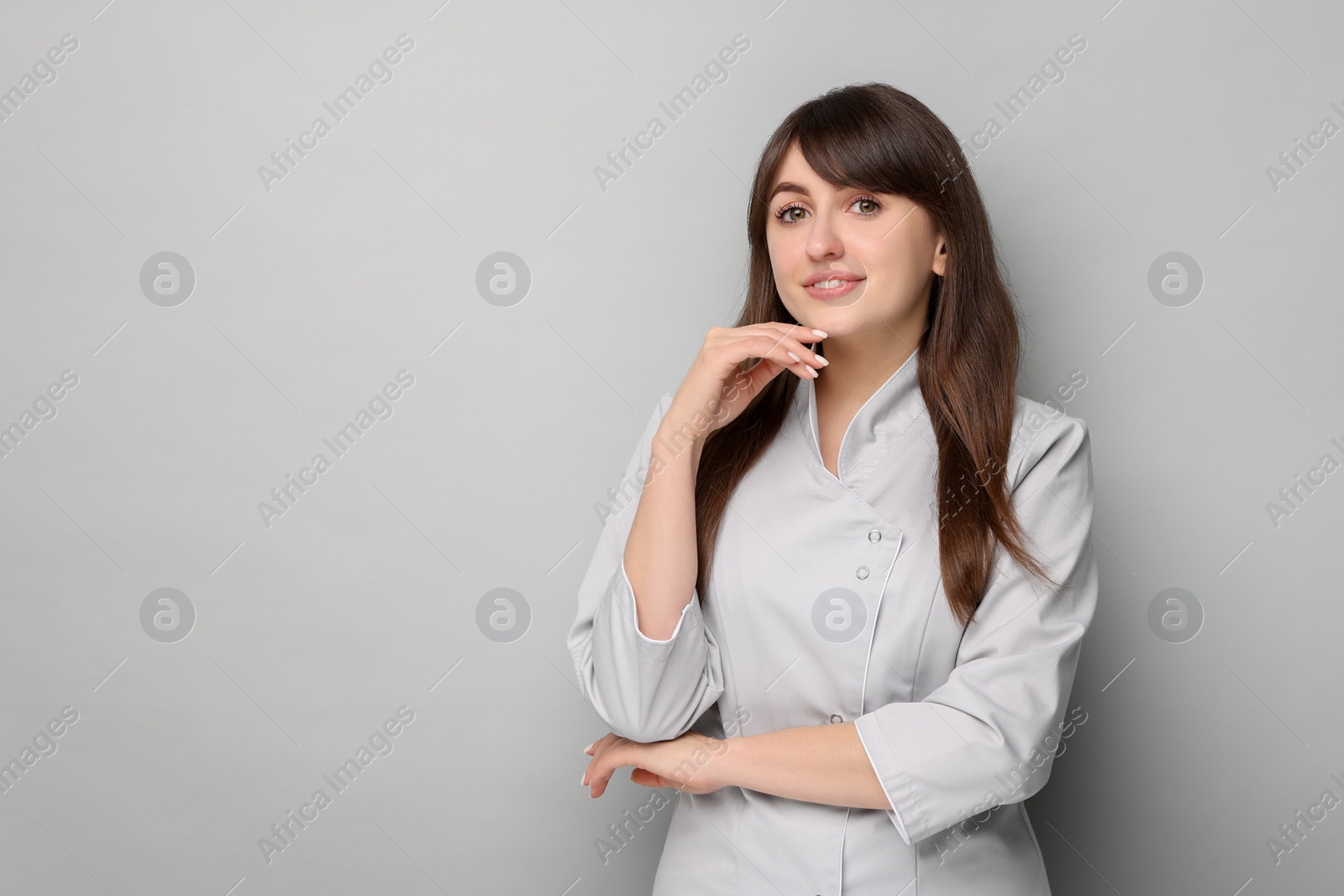 Photo of Cosmetologist in medical uniform on grey background, space for text