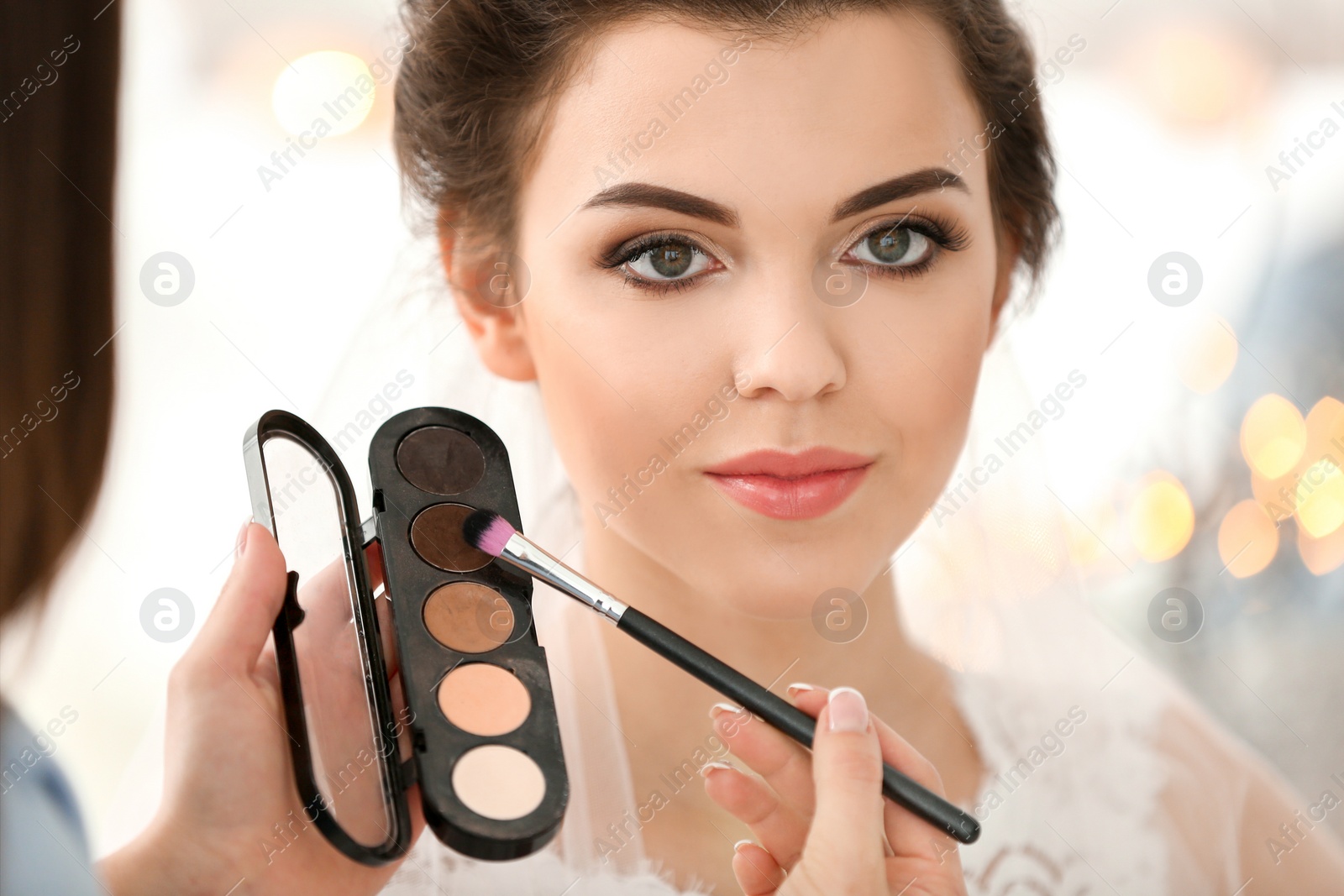 Photo of Makeup artist preparing bride before her wedding indoors