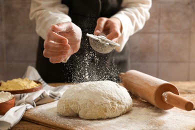 Photo of Woman sprinkling flour over dough at wooden table, closeup