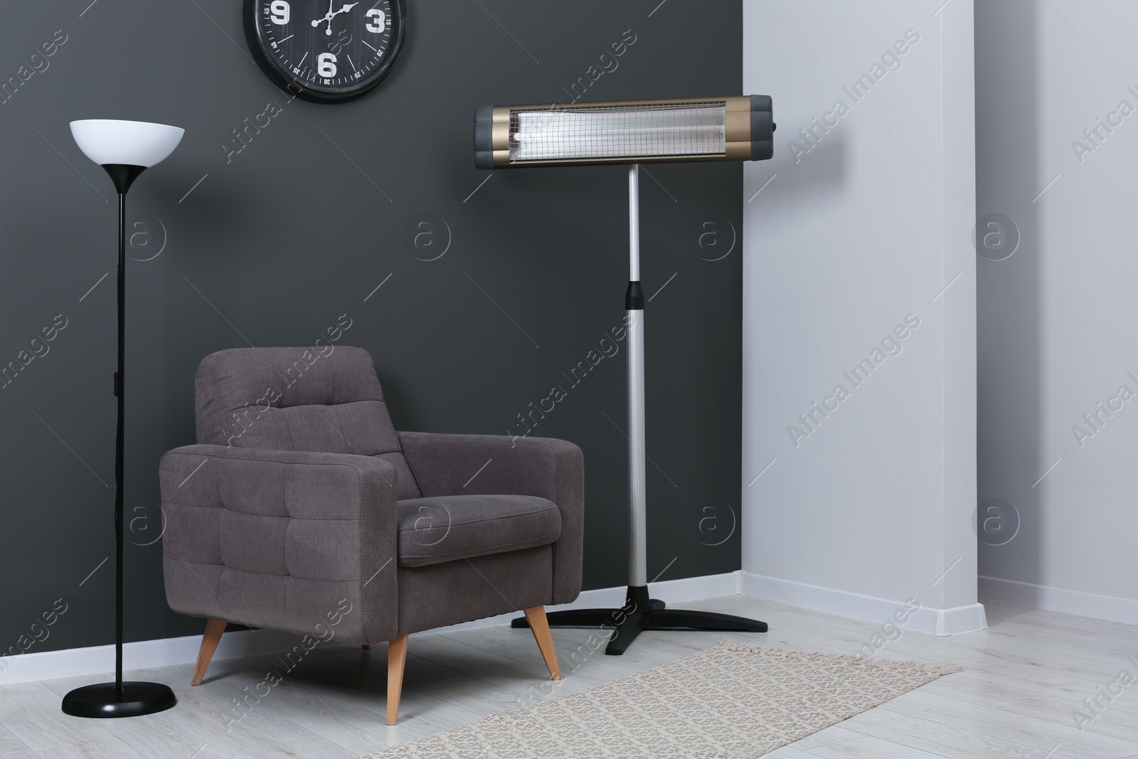 Photo of Electric infrared heater and stylish armchair in room