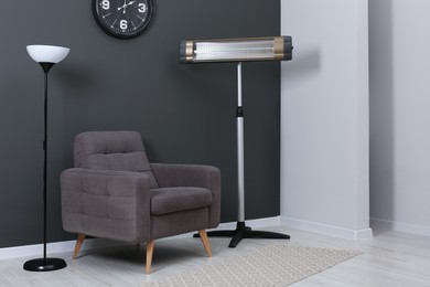 Photo of Electric infrared heater and stylish armchair in room