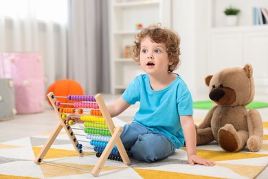 Cute little boy playing with wooden abacus on floor in kindergarten