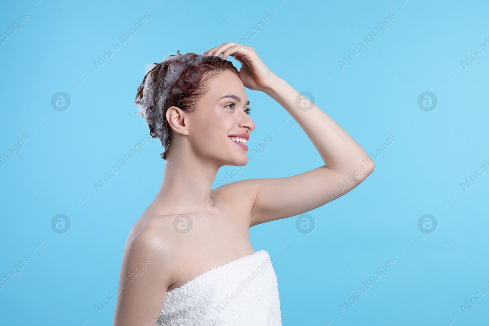 Photo of Happy young woman washing her hair with shampoo on light blue background